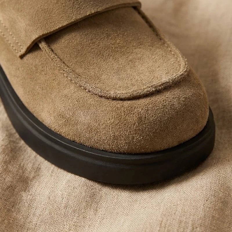 Avant des mules mocassin marron clair avec une  semelle noire sur un drap beige