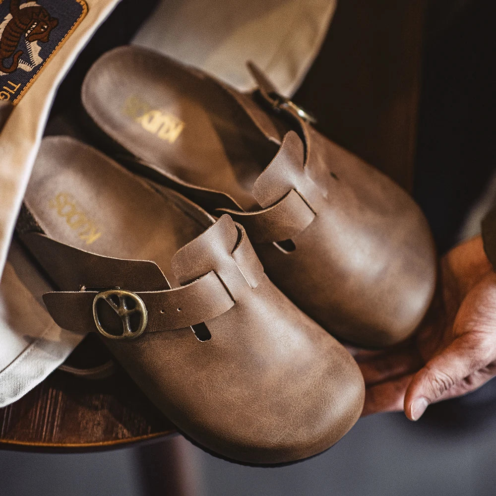 Mules cuir Crazy Horse marron posées sur une table touchant boucle bronze semelle liège visible