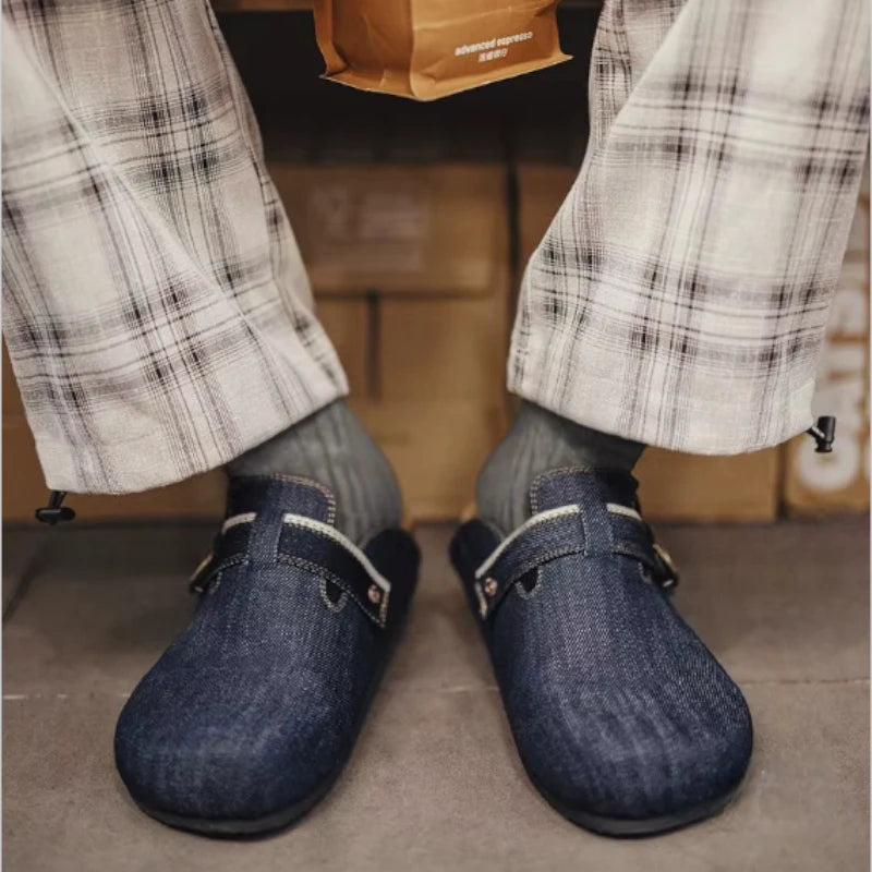 Vue de face d'une personne portant des mules en denim bleu marine pour homme avec un pantalon à carreaux et des chaussettes grises.
