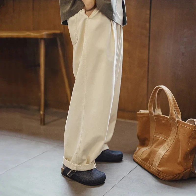 Vue latérale d'une personne et son outfit avec les mules en denim bleu marine et un pantalon chinos beige dans une pièce.