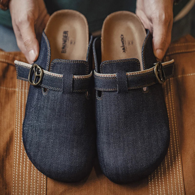 Mules en denim bleu foncé avec boucle métallique bronze tenues par des mains