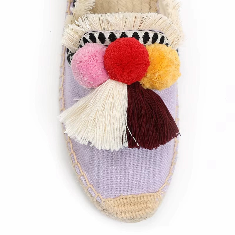 Gros plan sur l’avant d’une mule espadrille violette décorée de pompons colorés et franges textiles