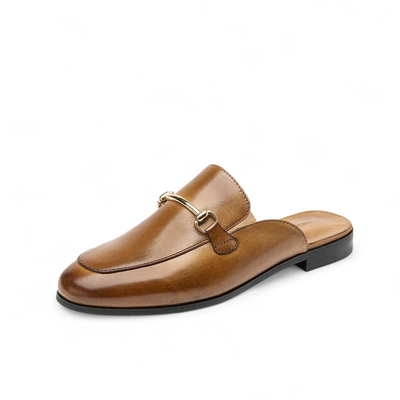 Mules Femme Chic en Cuir Marron posées de trois-quarts, avec détail métallique doré sur l’empeigne et semelle noire plate.