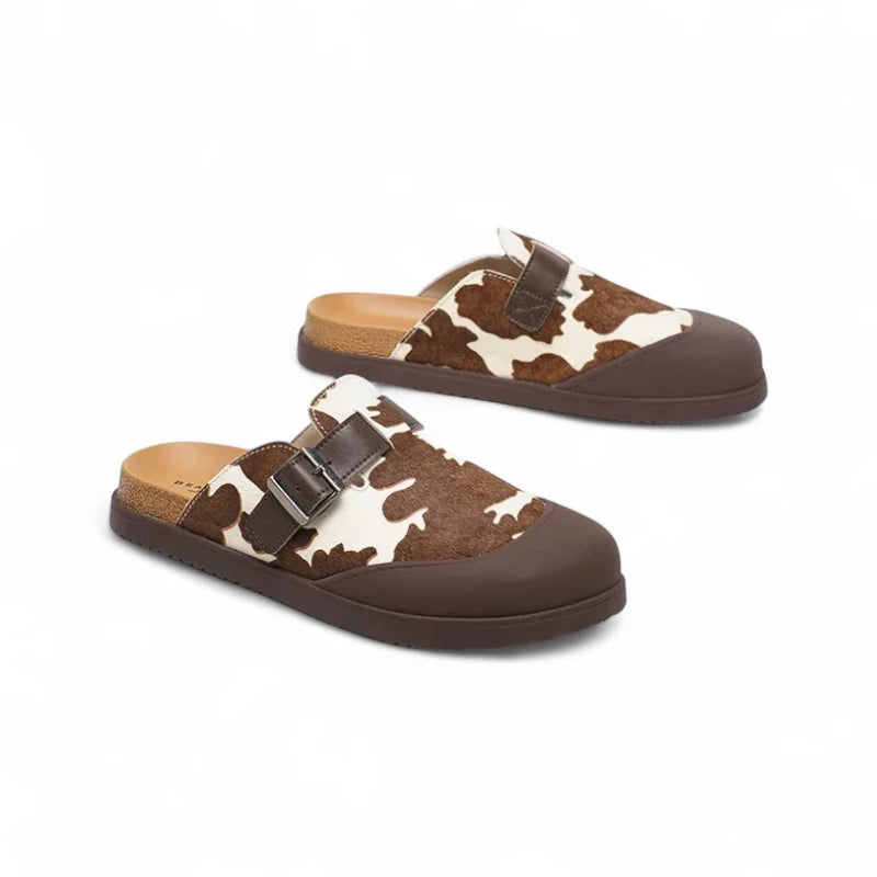 Mules Vache Marron et Beige pour femme posées en duo sur fond blanc, montrant leur imprimé vache marron et beige.
