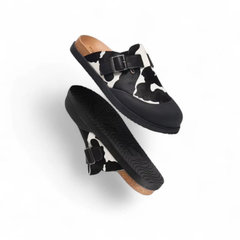 Mules Vache Noir et Beige femme en élévation, présentant la semelle extérieure caoutchouc et l’imprimé vache contrasté.